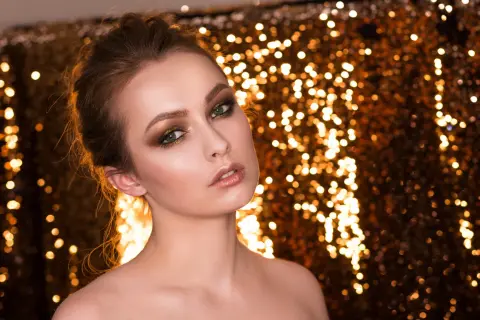 Oczy kobiety błyszczą jak złoto, a jej makijaż w odcieniach vanilla jaki to kolor podkreśla jej urodę na tle migoczących świateł.