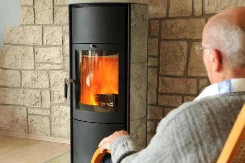 Älterer Mann sitzt vor einem brennenden Kaminofen. Die Idee, den Kamin stilllegen, kommt auf, wenn man ihn nicht mehr braucht.