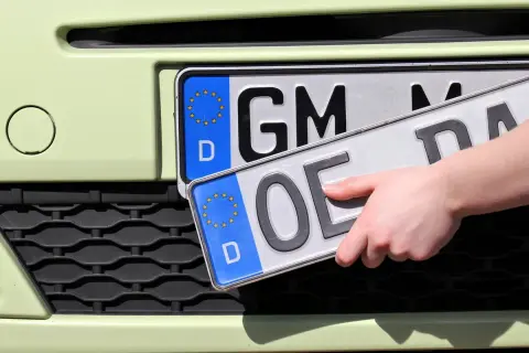 Dłoń trzyma nowe niemieckie tablice rejestracyjne. Jedna z nich ma oznaczenie "GM", druga "OE".