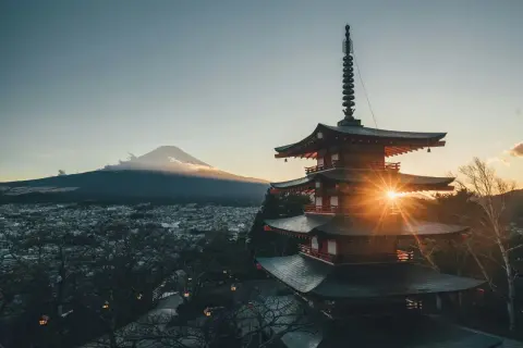 Zachód słońca nad Japonią. Góra Fudżi w chmurach, a przed nią pagoda rozświetlona promieniami słońca. Piękna pogoda.