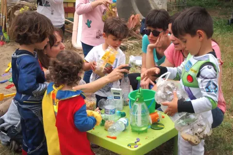 Niños disfrutan de actividades infantiles al aire libre, jugando con materiales reciclados y aprendiendo.