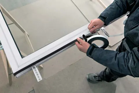 Pose porte fenêtre : application d'un joint d'étanchéité sur le cadre d'une fenêtre en aluminium.