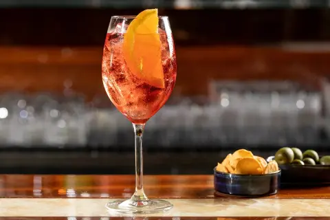 Un bicchiere di Spritz con fetta d'arancia, ghiaccio e stuzzichini. La spritz ricetta perfetta per l'aperitivo.