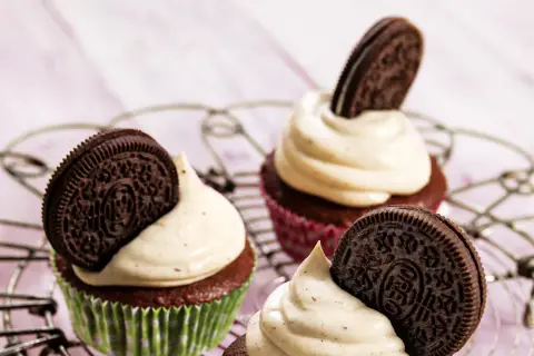 Drei leckere Oreo Muffins mit cremiger Glasur und einem Oreo-Keks obendrauf, auf einem Gitterrost arrangiert.