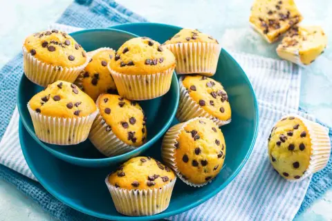 Muffin con gocce di cioccolato, dorati e invitanti, serviti in una ciotola blu.