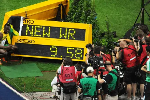Usain Bolt, najszybszy człowiek świata, świętuje nowy rekord świata 9.58s. Otoczony przez fotoreporterów, z flagą Jamajki.