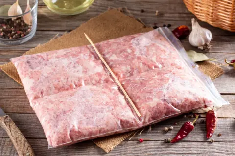 Zamrożone mięso mielone w woreczku, gotowe do rozmrożenia. Obok czosnek, pieprz i chili.