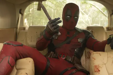 Deadpool, in seinem ikonischen roten Anzug, sitzt lässig im Auto und hält eine blutige Axt. Ein typischer Moment aus den Filmen von Ryan Reynolds.