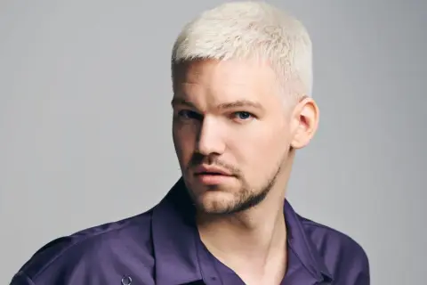 Mann mit platinblonden, kurz geschnittenen Haaren und einem Dreitagebart. Seine modernen herren frisuren unterstreichen seinen selbstbewussten Blick.