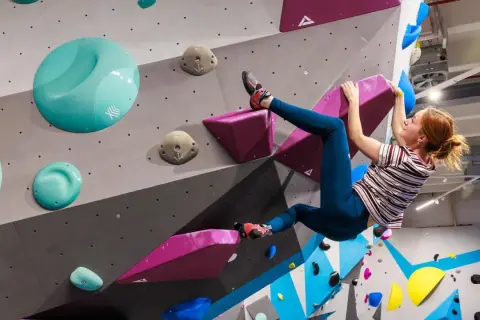 Frau klettert an einer bunten Wand in einer Boulderhalle in Hamburg. Sie hält sich an einem pinken Griff fest.