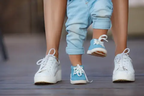 Dziecko w niebieskich bucikach i dorosły w białych sneakersach na drewnianym tarasie.