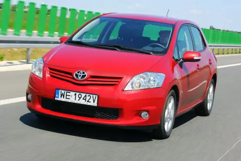 Czerwony Toyota Auris 2010 jedzie autostradą. Kierowca w czapce prowadzi auto.