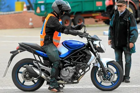 Młody motocyklista w kamizelce odblaskowej na placu manewrowym, obok instruktor. Zastanawia się, od ilu lat prawo jazdy jest wymagane na motocykl.