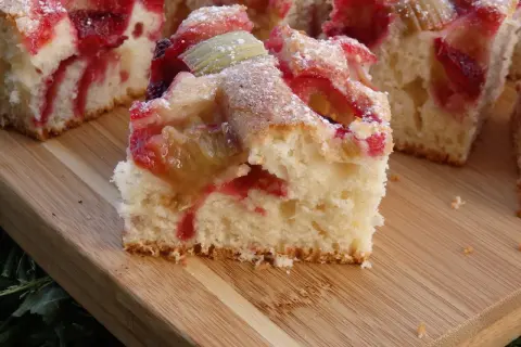 Puszyste ciasto na kefirze z rabarbarem i truskawkami, posypane cukrem pudrem. Idealne na letnie popołudnie.