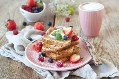 Ein Stapel goldbrauner French Toast, bestäubt mit Puderzucker, garniert mit Beeren und Sahne. Ein köstlicher Start in den Tag!