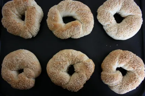 Sex gyllene simit, täckta med sesamfrön, ligger på en svart plåt. Perfekt för ett simit recept!
