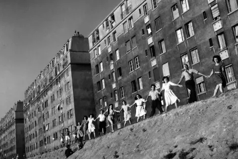 Une chaîne de jeunes gens se tient la main devant des immeubles, une scène de joie capturée dans cette photo célèbre.
