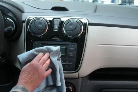 Ręka z szarą ściereczką czyści radio samochodowe i nawiewy. Dbałość o mycie detali w aucie.
