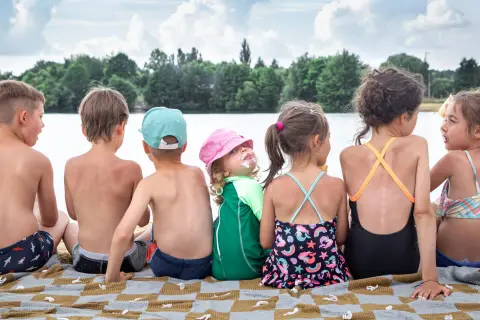 Siedmioro dzieci siedzi na kocu na plaży nad jeziorem, ciesząc się letnim dniem.