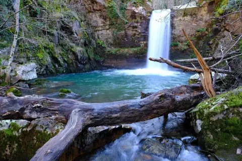 Impresionantes cascadas en Galicia, con un tronco caído en primer plano y aguas turquesas.