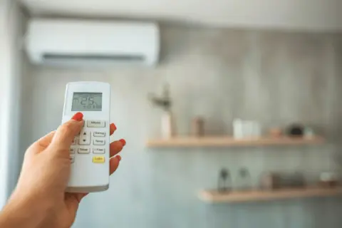 Main tenant ajuste la température de la climatisation pour un confort optimal, gérant la température clim été.