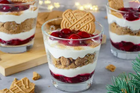 Festliche Desserts im Glas mit Kirschen, Kekskrümeln und Sahne, garniert mit Spekulatius.