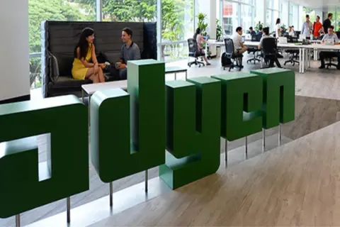 Zielone, przestrzenne litery z napisem "adyen" w nowoczesnym biurze. W tle ludzie pracują przy biurkach i rozmawiają.