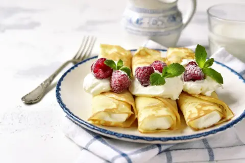 Pyszne naleśniki z mascarpone, udekorowane malinami i miętą, czekają na talerzu. Idealny deser na każdą okazję.