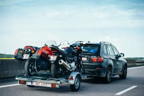 Deux motos sur une remorque tirée par une voiture sur l'autoroute. Le transport de ces véhicules nécessite un permis adéquat pour la catégorie de véhicule tracté.