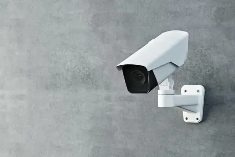 Une caméra de surveillance blanche est fixée sur un mur de béton. Cette caméra sans internet assure une sécurité discrète.