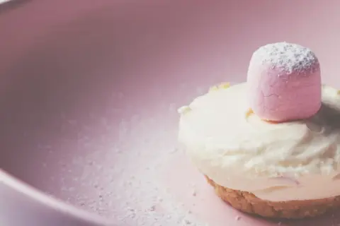 Delizioso namelaka al cioccolato bianco, con una soffice nuvola rosa in cima, adagiato su un piatto rosa cipria.
