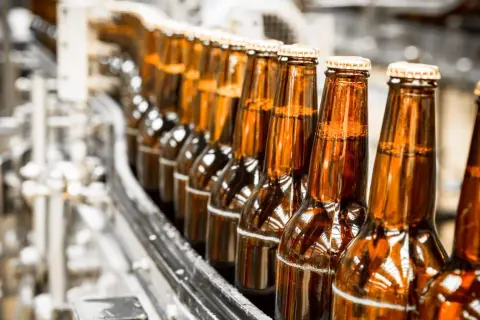 Rząd brązowych butelek piwa na linii produkcyjnej. Zastanawiasz się, ile kosztuje krata piwa?