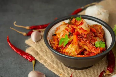 Miseczka z pikantnym kimchi, obok papryczki chili i czosnek. Idealne składniki, by dowiedzieć się, jak zrobić kimchi.