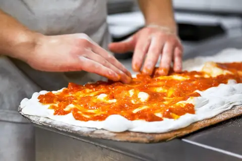 Händer sprider tomatsås på pizzadeg. En del av en matlagningskurs i att baka pizza.