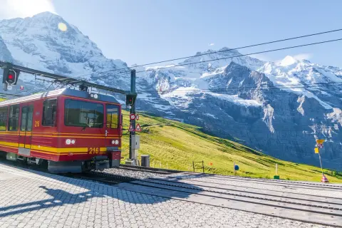 Treno rosso in montagna, pronto a salire tra vette innevate e verdi pendii.