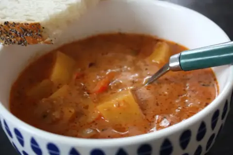 En skål med mustig cowboy soppa med potatis och en bit bröd.