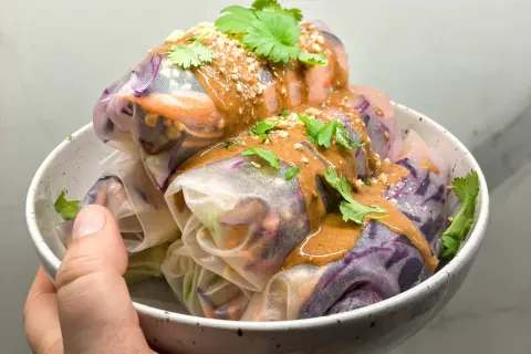 Kolorowe spring rolls z warzywami, polane kremowym sosem orzechowym i posypane orzeszkami. Idealne na lekki posiłek.