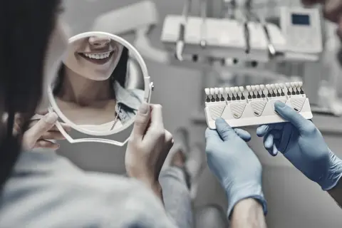 Stomatolog porównuje odcień zębów pacjentki z wzornikiem w gabinecie dentystycznym.
