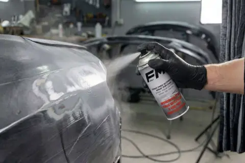 Mano enguantada aplica imprimación en spray a un coche. Se puede dar imprimación encima de pintura para un acabado perfecto.