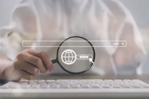 Dłoń z lupą bada ikonę globu i "www" podświetloną na tle paska wyszukiwania. Kluczowe dla **techniczne seo**.