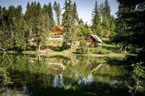 Reflets parfaits des chalets et des sapins dans le lac du Poursollet, un paysage de montagne paisible.