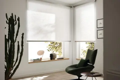 Moderne Sichtschutz-Fenster-Innen-Ideen: Helle Rollos mit dezentem Muster schaffen Privatsphäre und lassen Licht herein. Ein grüner Sessel lädt zum Entspannen ein.
