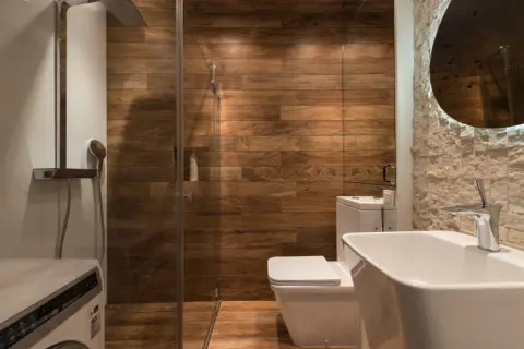 Moderno baño con ducha de cristal, paredes de madera y lavabo. ¿Cuánto cuesta cambiar bañera por plato de ducha?