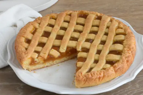 Crostata con marmellata, un classico della crostata ricetta tradizionale, servita su un piatto bianco con un tovagliolo di lino.
