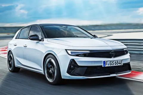 Biały Opel Astra GSe pędzi po torze wyścigowym, z kołami w ruchu, na tle błękitnego nieba.