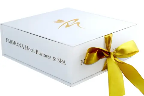 Eleganckie białe pudełko z logo Farmona Hotel Business & SPA, przewiązane złotą wstążką. Idealne na bon do spa.