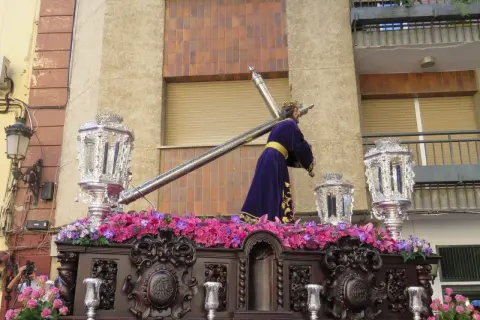 Procesión de Semana Santa con imagen de Jesús portando la cruz, adornada con flores y candelabros. Obra de Amadeo Ruiz Olmos.
