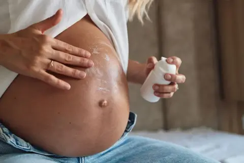 Manos aplicando crema en el vientre de una mujer embarazada. La crema, con un toque de rosa mosqueta, ayuda a cuidar la piel.