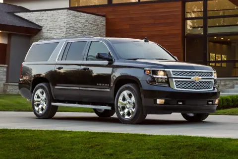 Czarny Chevrolet Suburban na podjeździe przed nowoczesnym, podmiejskim domem z kamiennymi i drewnianymi elementami.