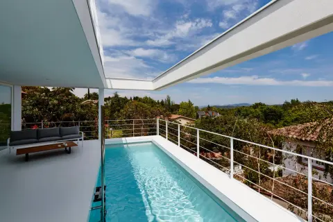 Una moderna piscina en ático con vistas a un paisaje verde. Un sofá gris y una mesa de centro completan el espacio.
